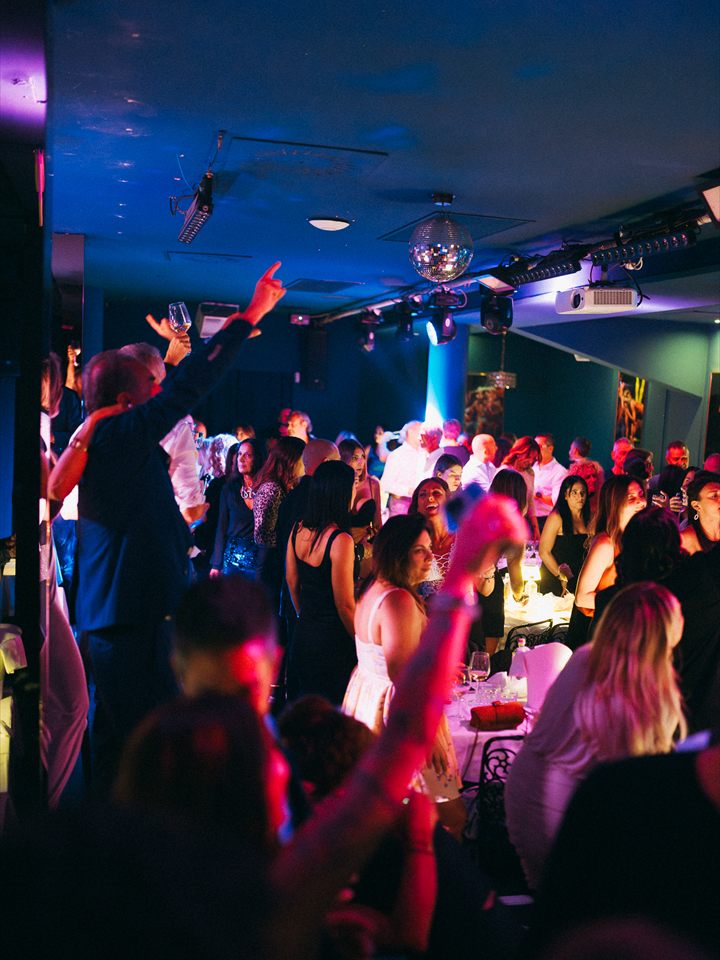 La sala durante la serata, con gli ospiti in piedi sotto la palla a specchi e il proiettore